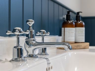 A bathroom sink with chrome faucet and two brown pump bottles on a wooden tray against blue paneling at Stags Mount in Thornton Dale