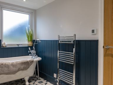 A bathroom with a clawfoot bathtub, a towel warmer, a wooden door, a frosted window with a plant on the sill and tiled floor at Stags Mount in Thornton Dale