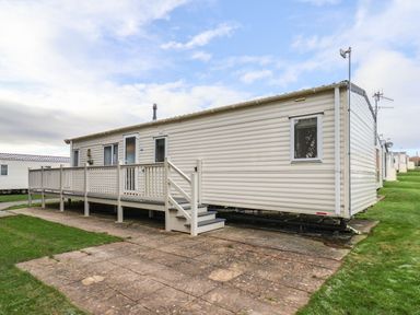 A beige mobile home with a small porch and steps on a paved area with grass around at Forest Star in Cayton