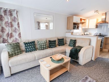 A living room with a beige sofa with green pillows a wooden coffee table and a kitchen in the background at Forest Star in Cayton