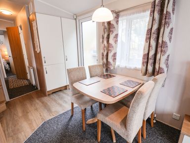 A dining area with a wooden table and four upholstered chairs next to a window with patterned curtains at Forest Star in Cayton
