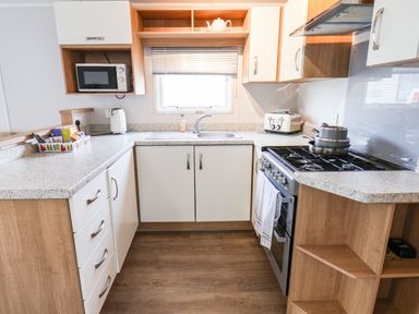 A kitchen with white cabinets wooden shelves a microwave kettle toaster stove and sink at Forest Star in Cayton