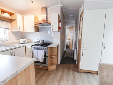A kitchen with a stove sink toaster cabinets and a hallway leading to a bedroom at Forest Star in Cayton