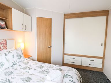 A bedroom with a bed with leafy patterned bedding a wooden door white cupboards and a wardrobe at Forest Star in Cayton