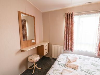 A bedroom with a bed topped with folded towels a small dressing table with a mirror and a round stool next to a window with patterned curtains at Forest Star in Cayton