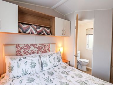 A bedroom with a bed with patterned bedding a bedside table a lamp and an open door leading to a bathroom at Forest Star in Cayton