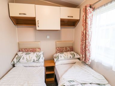 A bedroom with two single beds separated by a wooden nightstand and overhead cabinets at Forest Star in Cayton