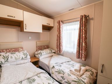 A bedroom with two single beds with botanical bedding a window with patterned curtains and overhead storage at Forest Star in Cayton