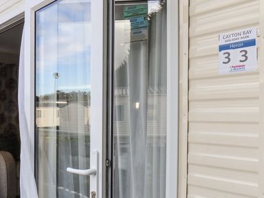 A white door with sheer curtains next to a sign reading Cayton Bay Holiday Park Heron 33 at Forest Star in Cayton