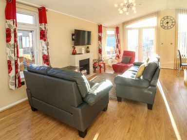 A living room with two sofas a red chair a wall-mounted TV and large windows at Dream Catcher Lodge in Carnforth