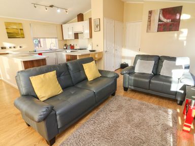 A living room with two black leather sofas and a kitchen area in the background at Dream Catcher Lodge in Carnforth