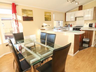 A dining area with a glass table and six black chairs next to a kitchen with white cabinets at Dream Catcher Lodge in Carnforth