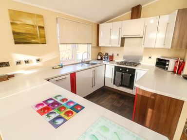A kitchen with white cabinets a sink a gas stove toaster microwave and kettle at Dream Catcher Lodge in Carnforth