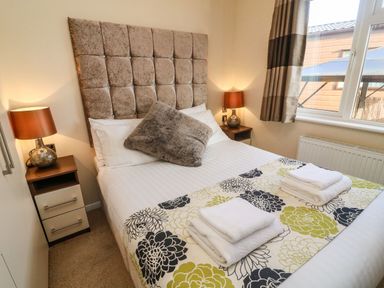 A bedroom with a bed headboard bedside tables with lamps and folded towels on bed at Dream Catcher Lodge in Carnforth
