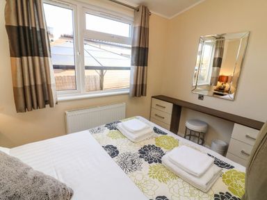 A bedroom with a bed folded towels a window with curtains a radiator a dressing table a mirror and a stool at Dream Catcher Lodge in Carnforth