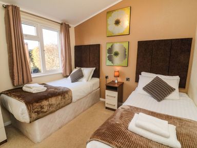 A bedroom with two single beds a nightstand with a lamp and two framed floral pictures on the wall at Dream Catcher Lodge in Carnforth