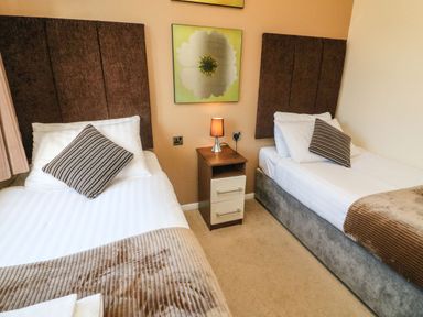 A bedroom with two single beds and a nightstand with a lamp and a flower painting at Dream Catcher Lodge in Carnforth