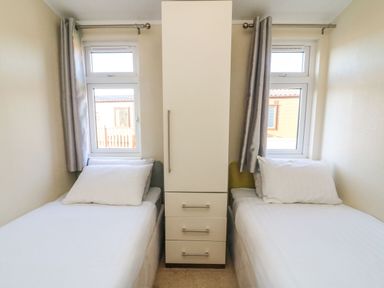 A bedroom with two single beds separated by a white wardrobe and windows behind the beds at Dream Catcher Lodge in Carnforth