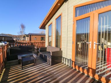 A wooden deck with outdoor wicker furniture and glass doors at Dream Catcher Lodge in Carnforth