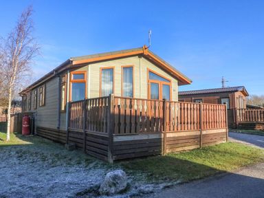 A wooden cabin with a fenced porch on a grassy area at Dream Catcher Lodge in Carnforth