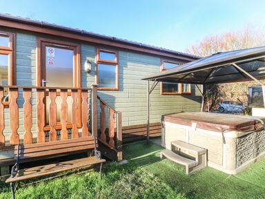 An outdoor area with a wooden bench a hot tub with a cover and steps and a wooden side door with windows at Dream Catcher Lodge in Carnforth
