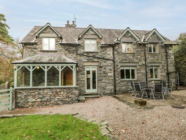 A stone house with green framed windows and doors and an outdoor patio with a table and chairs at Scandale Bridge Cottage in Ambleside