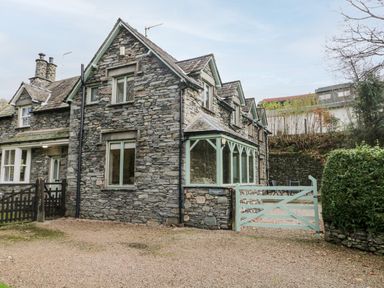 A stone exterior house with multiple windows and a green wooden gate at Scandale Bridge Cottage in Ambleside
