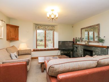 A living room with sofas a wooden coffee table a television and a window seat at Scandale Bridge Cottage in Ambleside