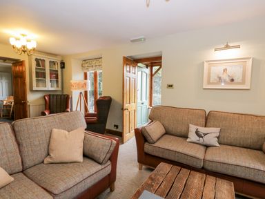 A living room with two fabric sofas a wooden coffee table armchairs a floor lamp and bookshelf at Scandale Bridge Cottage Ambleside