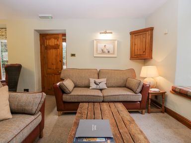 A sitting room with sofas a wooden coffee table a lamp and a wooden door at Scandale Bridge Cottage in Ambleside