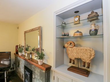 A living room corner with a stone fireplace mantel holding plants and a clock next to a built-in shelf with pottery and a wooden ram at Scandale Bridge Cottage in Ambleside