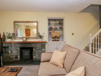 A living room with a stone fireplace a wooden mantle a mirror plants a wooden sculpture on shelves and a sofa with cushions at Scandale Bridge Cottage in Ambleside