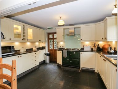A kitchen with cream cabinets black countertops a green stove and a wooden door at Scandale Bridge Cottage in Ambleside