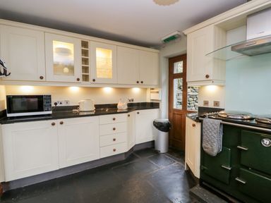 A kitchen with white cabinets microwave toaster wood door and green stove at Scandale Bridge Cottage in Ambleside