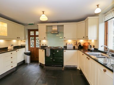 A kitchen with cream cabinets black countertops a green stove and a wooden door at Scandale Bridge Cottage in Ambleside