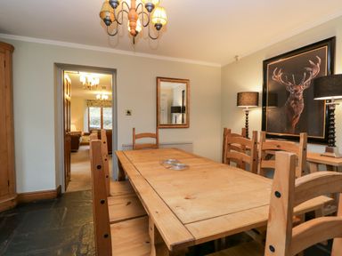 A dining room with a wooden table and chairs a mirror on the wall and a framed picture of a stag at Scandale Bridge Cottage in Ambleside