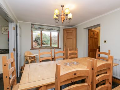 A dining room with a wooden table and chairs a high chair a wooden cupboard and a window with a blind at Scandale Bridge Cottage Ambleside