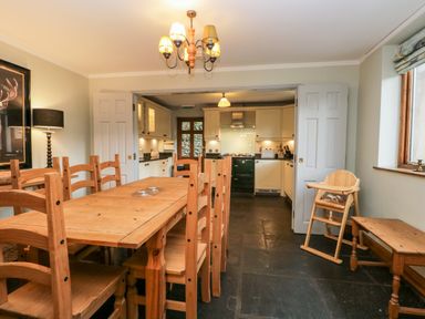 A dining room with a wooden table and chairs next to a kitchen with cream cabinets and a green stove at Scandale Bridge Cottage in Ambleside