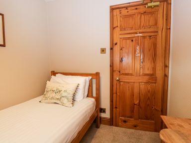 A small bedroom with a single bed a wooden door and a wooden table at Scandale Bridge Cottage in Ambleside