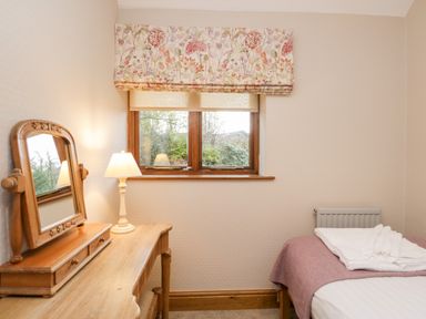 A bedroom with a wooden dressing table and mirror a lamp and a bed with folded towels at Scandale Bridge Cottage in Ambleside