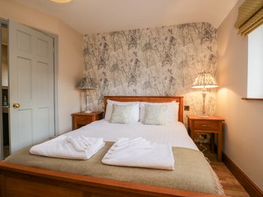 A bedroom with a wooden bed white linens bedside tables and lamps at Scandale Bridge Cottage Ambleside