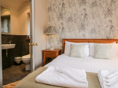 A bedroom with a wooden bed green patterned pillows bedside table with lamp and an en suite bathroom at Scandale Bridge Cottage in Ambleside