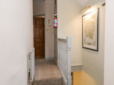 A narrow hallway with carpeted floor a white wooden railing a framed picture on the wall and a wooden door at Scandale Bridge Cottage in Ambleside