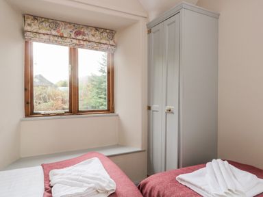 A bedroom with two single beds with folded towels on them a window with floral blinds and a grey wardrobe at Scandale Bridge Cottage in Ambleside