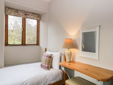 A bedroom with a single bed a wooden desk lamp and mirror at Scandale Bridge Cottage in Ambleside