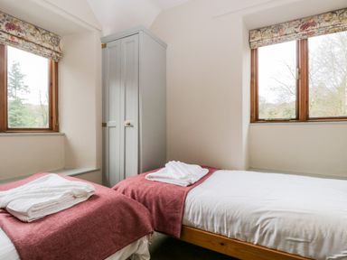 A bedroom with two single beds and folded towels near two windows at Scandale Bridge Cottage in Ambleside