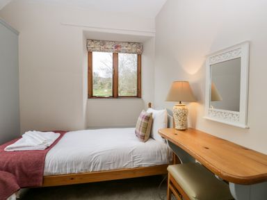 A bedroom with a single bed beside a window and a wooden desk with a lamp and mirror at Scandale Bridge Cottage in Ambleside