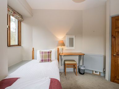 A bedroom with a single bed a wooden desk with a lamp and stool next to a window at Scandale Bridge Cottage in Ambleside