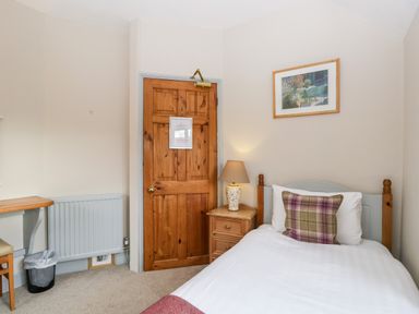 A bedroom with a single bed a bedside table with lamp a wooden door a framed picture and a desk with chair at Scandale Bridge Cottage Ambleside