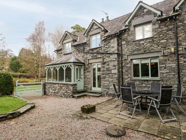 An exterior stone house with outdoor seating and a small enclosed porch at Scandale Bridge Cottage in Ambleside